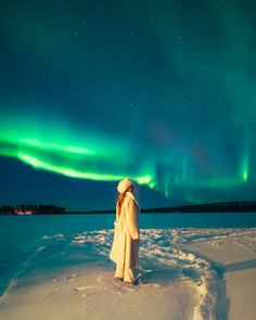 a woman standing in the snow looking at the aurora bore