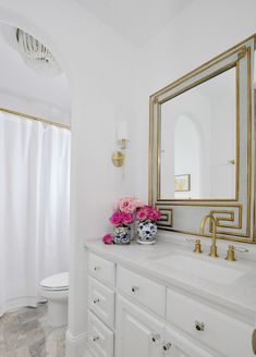 a white and gold bathroom with flowers on the counter