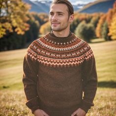 a man standing in the grass with his hands in his pockets and wearing a sweater