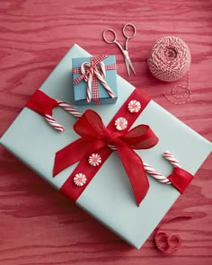 a present wrapped in blue paper with red ribbon and candy canes next to it