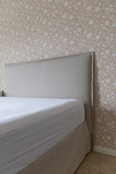 a white bed sitting in a bedroom next to a wall with floral designs on it