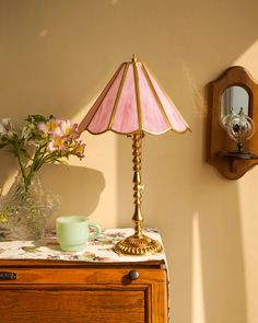 a pink lamp sitting on top of a wooden dresser next to a vase with flowers