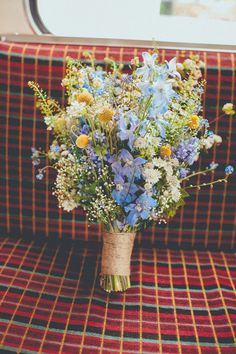 a bouquet of wildflowers is sitting on a plaid couch in front of a window