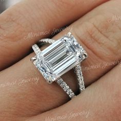 a woman's engagement ring with an emerald cut diamond in the center and pave diamonds around it