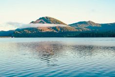 a lake with mountains in the background and clouds hanging over it's head,