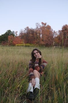 a young woman sitting in the grass with her hands on her chin and looking at the camera