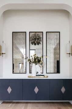 two mirrors are hanging on the wall above a blue cabinet with gold accents and vases