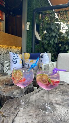 two wine glasses filled with pink liquid and garnished with lemons on a wooden table