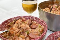 two red bowls filled with rice and sausage next to a metal pan full of food