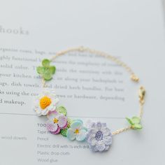 a bracelet with crocheted flowers on it sitting on top of an open book