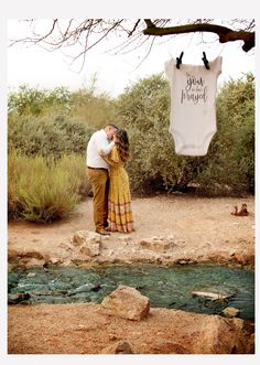 a man and woman kissing in front of a body of water with a t - shirt hanging from the clothes line