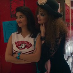 two young women standing next to each other in front of lockers with writing on them