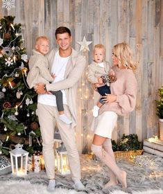 a man and woman holding two children in front of a christmas tree with lights on it