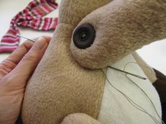 a person holding a brown teddy bear with pins in it's ear and thread