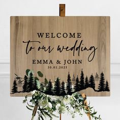 a wooden sign with the words welcome to our wedding on it and some greenery