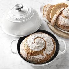 a loaf of bread sitting in a pan next to a white dutch oven on top of a marble counter