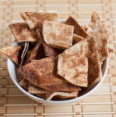 a white bowl filled with tortilla chips on top of a bamboo place mat