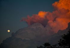 the moon is setting behind some clouds in the sky