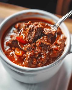 a spoon full of chili beef soup on top of a table