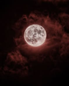 the full moon is seen through clouds on a dark night with red light in the sky