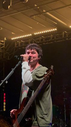 a man holding a bass in front of a microphone and singing into a mic on stage