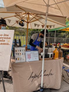 a man standing behind a table with an open umbrella over it that has a sign on it