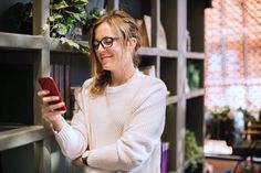 a woman standing in front of a book shelf holding a cell phone and looking at the screen