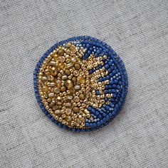 a blue and gold beaded brooch sitting on top of a gray cloth