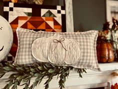 a decorative pillow on top of a mantle with pumpkins and greenery in the background