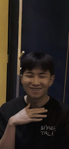 a young man smiles as he stands in front of a door with his hands on his chest