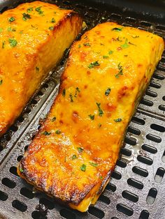 two pieces of cheese covered meat cooking on a grill grate with parsley sprinkled on top