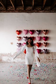 a woman in a white dress is walking through confetti covered room with hearts on the wall