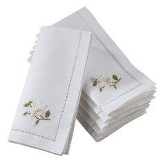 four white napkins with embroidered flowers on them are stacked up in front of each other