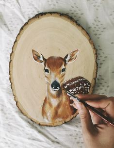 someone is painting a deer on a wood slice