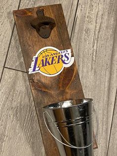 a metal bucket sitting on top of a wooden shelf next to a sign that says it's lakers