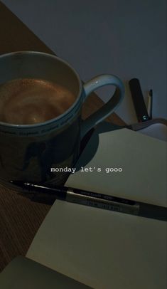 a cup of coffee sitting on top of a desk next to a pen and paper