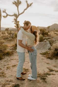 a man and woman standing in the desert with joshua tree behind them, kissing each other