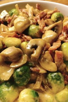 a white bowl filled with broccoli and mushrooms covered in sauce on top of a wooden table