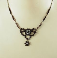 A charming antique Victorian Georgian style Bohemian garnet and paste festoon necklace in pinchbeck or tombak. The central floral cluster, 6mm in diameter, with six circular pastes, each 3mm in diameter, with a surround of rose cut garnets. In a bow shaped setting with further rose cut garnets. With a floral drop with a central paste and six rose cut garnets.  The chain with three groups of five, three and four garnets to each side.  With a fully closed back fastening. On an oval link chain. Wit Rose Dans, Festoon Necklace, Group Of Five, Bib Necklaces, Antique Necklace, Love Knot, Antique Finish, Antique Victorian, Spring Rings