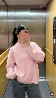 a woman taking a selfie in front of an elevator with her pink sweater on