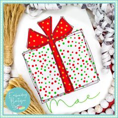 a cross - stitch christmas present with red ribbon and green polka dots on white fabric