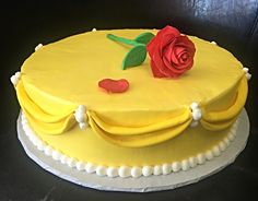 a yellow frosted cake with a red rose on top and white trimmings