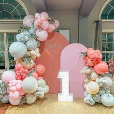 balloons are arranged around the number one balloon arch for a first birthday party in pink, white and silver