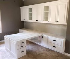 a white desk sitting in the middle of a room next to a window and cupboards