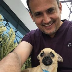 a man is holding a small dog in his lap and smiling at the camera,