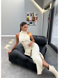 a woman sitting on top of a black chair in an office building wearing a white dress