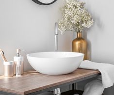 a white bowl sink sitting on top of a wooden counter next to a vase with baby's breath