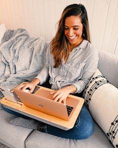 a woman sitting on a couch with a laptop computer in her lap and smiling at the camera