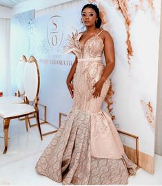 a woman standing in front of a white wall wearing a pink and gold gown with feathers on it