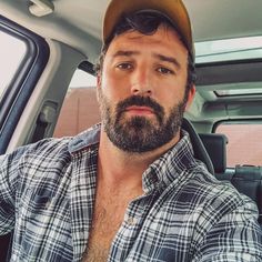 a man with a beard wearing a hat in the back seat of a car looking at the camera